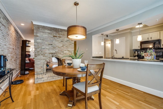 dining area with ornamental molding, brick wall, sink, and light hardwood / wood-style flooring