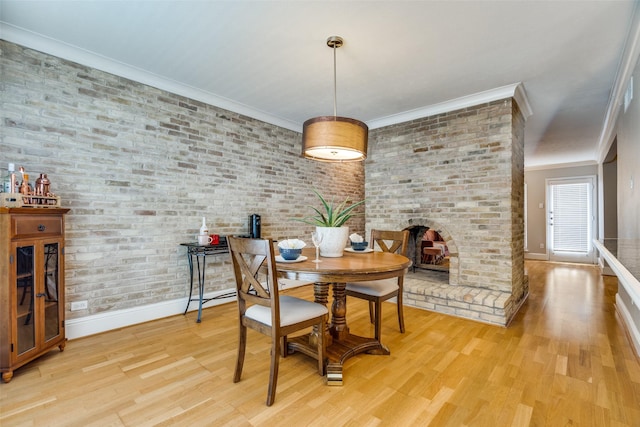 dining space featuring crown molding, a fireplace, light hardwood / wood-style floors, and brick wall