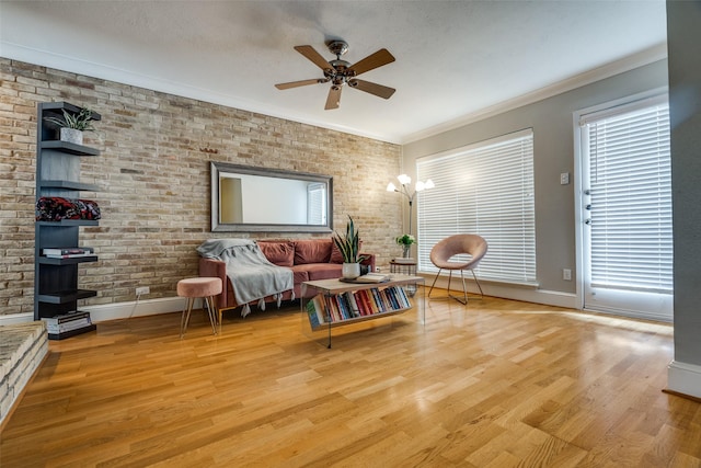 living room with crown molding, light hardwood / wood-style floors, ceiling fan, and brick wall