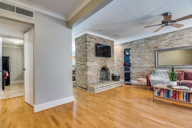 living room with crown molding, wood-type flooring, ceiling fan, brick wall, and a fireplace