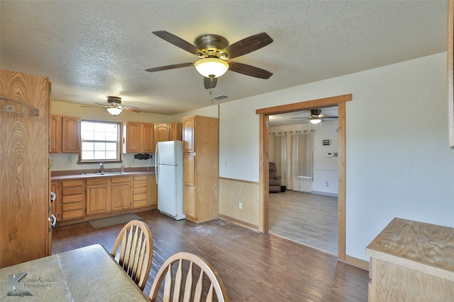 kitchen with a textured ceiling, white refrigerator, wooden walls, sink, and dark hardwood / wood-style floors