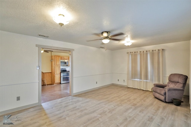 living area with a textured ceiling, light hardwood / wood-style flooring, and ceiling fan