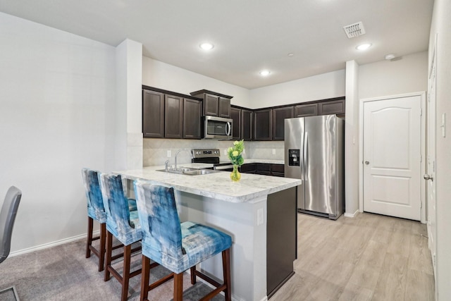 kitchen with kitchen peninsula, dark brown cabinets, appliances with stainless steel finishes, sink, and a breakfast bar area