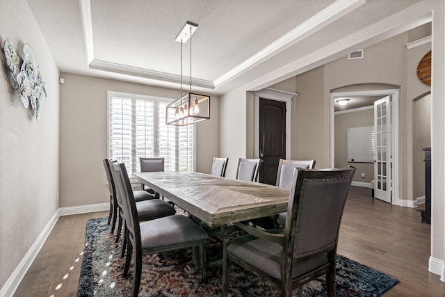 dining space with ornamental molding, a textured ceiling, dark hardwood / wood-style flooring, and a raised ceiling