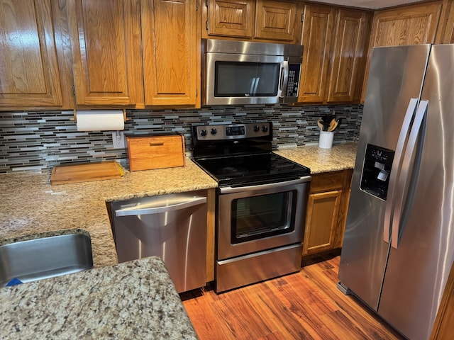 kitchen with tasteful backsplash, hardwood / wood-style floors, light stone countertops, and appliances with stainless steel finishes