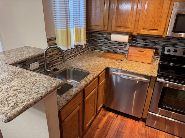 kitchen with sink, light stone counters, dark hardwood / wood-style flooring, stainless steel appliances, and backsplash