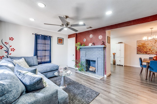 living room with wood-type flooring, a brick fireplace, and ceiling fan with notable chandelier