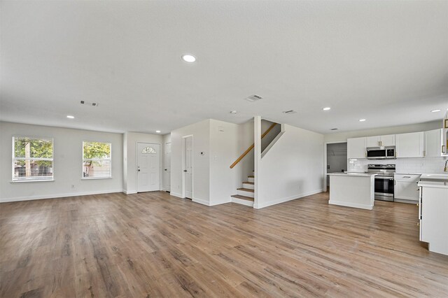 kitchen with tasteful backsplash, white cabinets, a kitchen island, light wood-type flooring, and stainless steel appliances