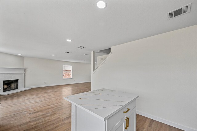 interior space with a center island, white cabinetry, a fireplace, light hardwood / wood-style floors, and light stone counters