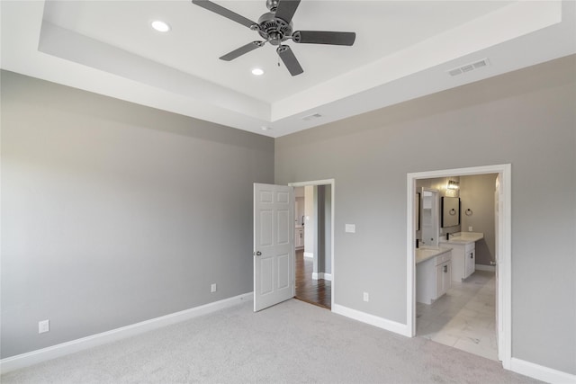 unfurnished bedroom featuring light colored carpet, ensuite bath, ceiling fan, and a raised ceiling