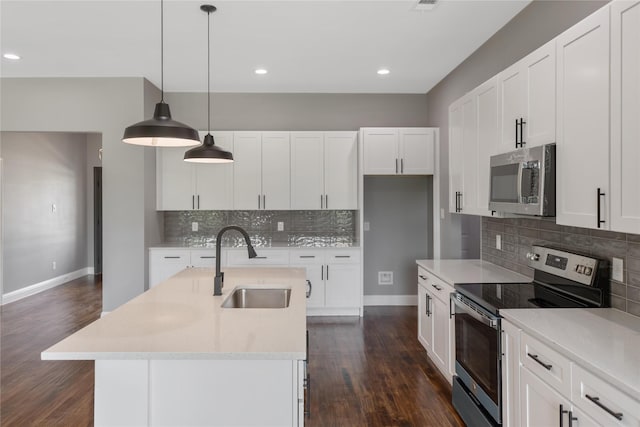 kitchen featuring white cabinetry, sink, decorative light fixtures, stainless steel appliances, and a center island with sink