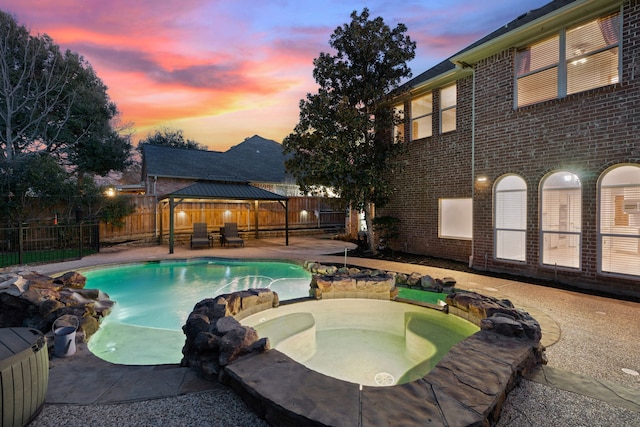 pool at dusk featuring an in ground hot tub and a gazebo