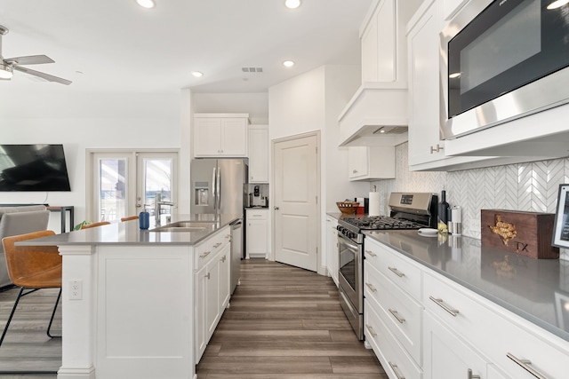 kitchen featuring a breakfast bar area, stainless steel appliances, white cabinets, a center island with sink, and decorative backsplash