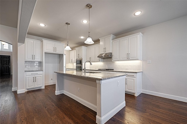 kitchen featuring an island with sink, sink, dark stone countertops, and white cabinets