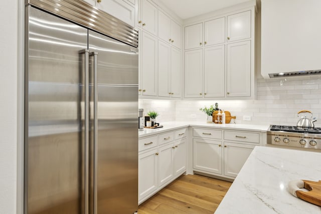 kitchen featuring light hardwood / wood-style flooring, appliances with stainless steel finishes, white cabinetry, light stone counters, and decorative backsplash