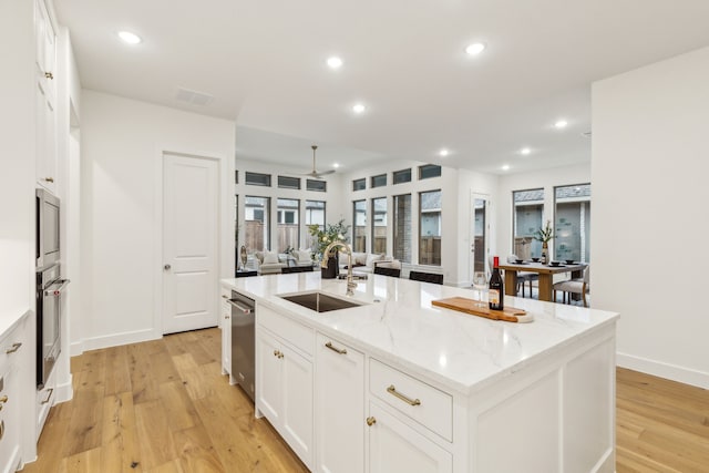 kitchen with sink, white cabinetry, stainless steel appliances, light stone countertops, and an island with sink