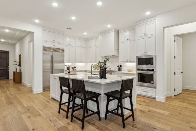 kitchen with white cabinets, built in appliances, and wall chimney range hood