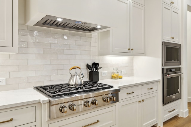 kitchen with white cabinetry, ventilation hood, stainless steel appliances, light stone countertops, and decorative backsplash