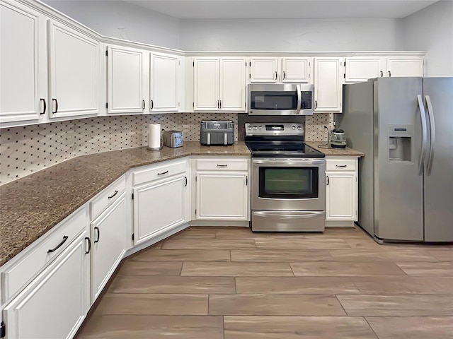 kitchen featuring tasteful backsplash, appliances with stainless steel finishes, white cabinets, and dark stone counters