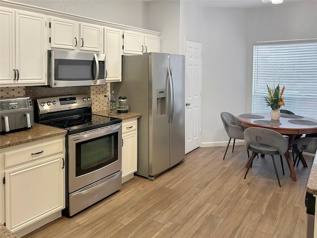 kitchen featuring backsplash, stainless steel appliances, white cabinets, and light wood-type flooring