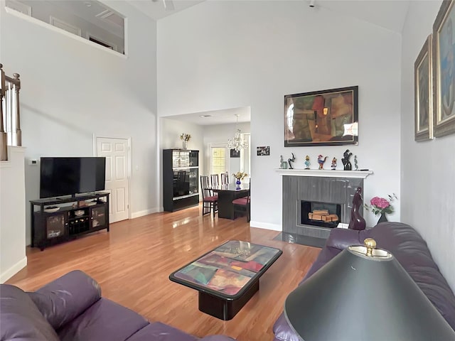 living room featuring an inviting chandelier, hardwood / wood-style flooring, a premium fireplace, and a high ceiling