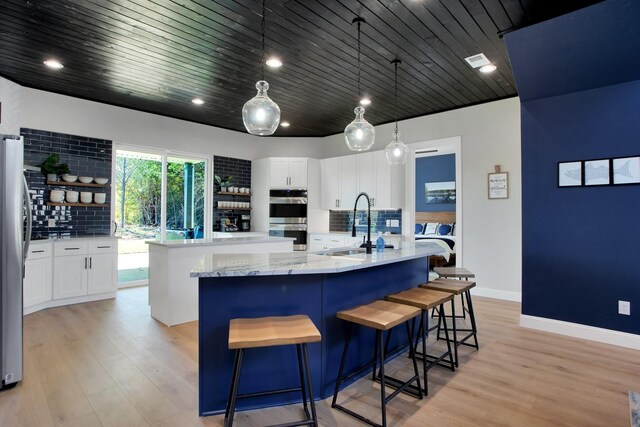 kitchen with appliances with stainless steel finishes, white cabinetry, decorative backsplash, decorative light fixtures, and an island with sink