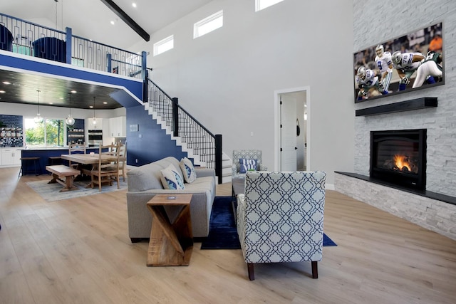 living room with beamed ceiling, a high ceiling, light hardwood / wood-style flooring, and a fireplace