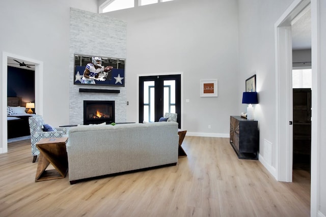 living room with a stone fireplace, a high ceiling, and light hardwood / wood-style flooring