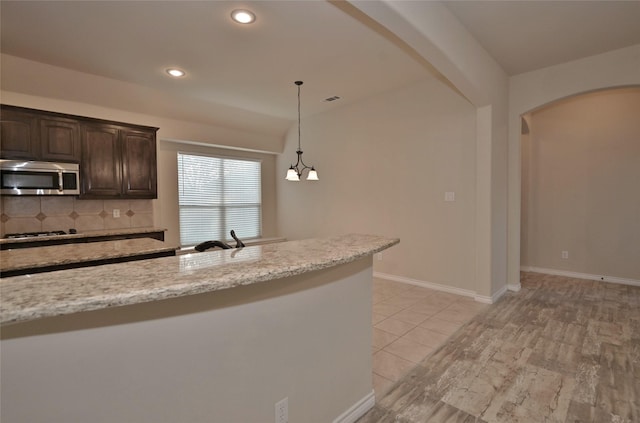 kitchen with decorative backsplash, sink, dark brown cabinetry, pendant lighting, and light stone counters