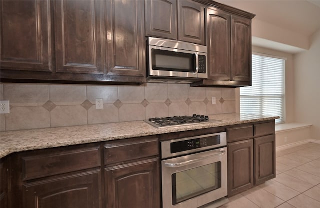 kitchen featuring light stone countertops, appliances with stainless steel finishes, tasteful backsplash, dark brown cabinets, and light tile patterned flooring