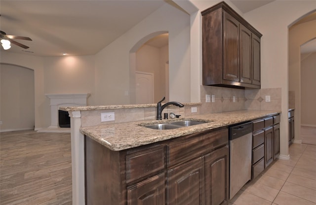 kitchen with dark brown cabinets, stainless steel dishwasher, sink, light tile patterned floors, and light stone countertops