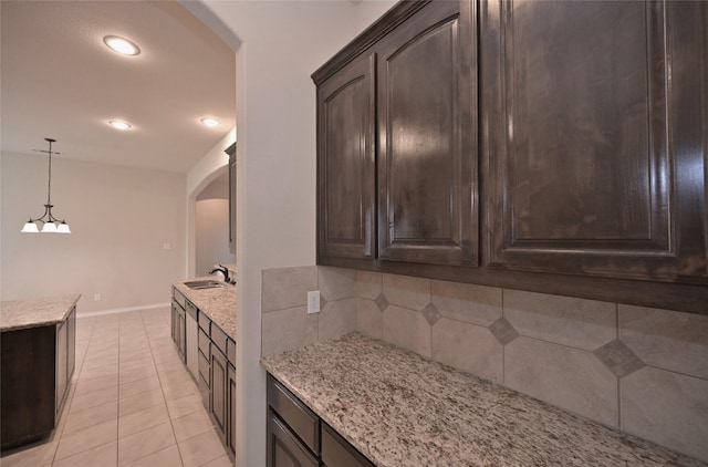 kitchen with sink, backsplash, dark brown cabinetry, and light stone countertops