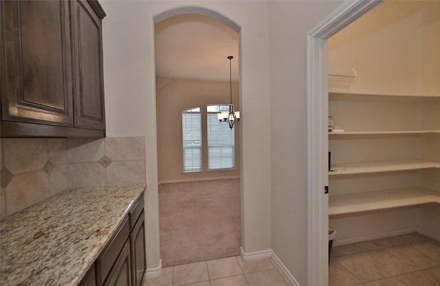 kitchen featuring light stone counters, light tile patterned floors, decorative backsplash, and dark brown cabinetry