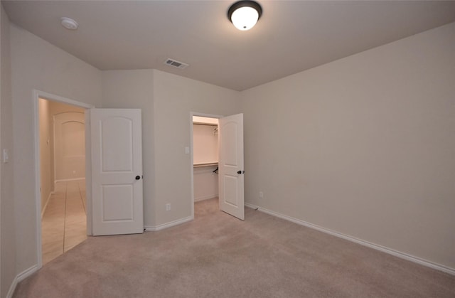 unfurnished bedroom with a closet, light colored carpet, and a spacious closet