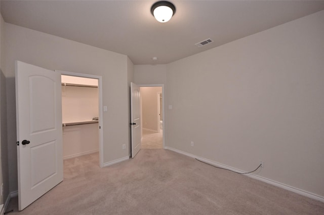 unfurnished bedroom featuring a walk in closet, light colored carpet, and a closet