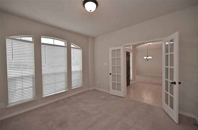 spare room featuring a chandelier, french doors, and light carpet