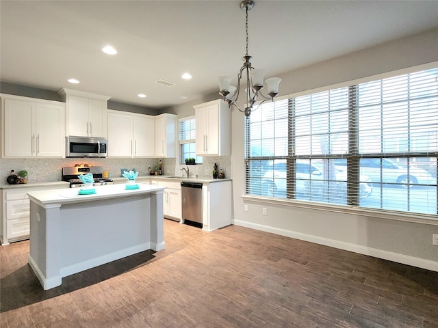 kitchen with hanging light fixtures, appliances with stainless steel finishes, white cabinets, hardwood / wood-style floors, and a center island