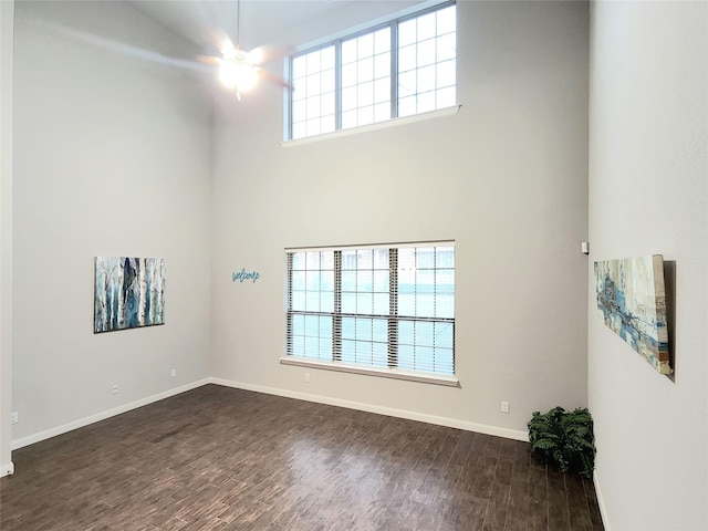 unfurnished room featuring ceiling fan, dark hardwood / wood-style floors, and a towering ceiling