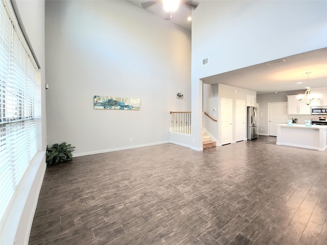 unfurnished living room featuring a high ceiling, ceiling fan, and dark hardwood / wood-style flooring