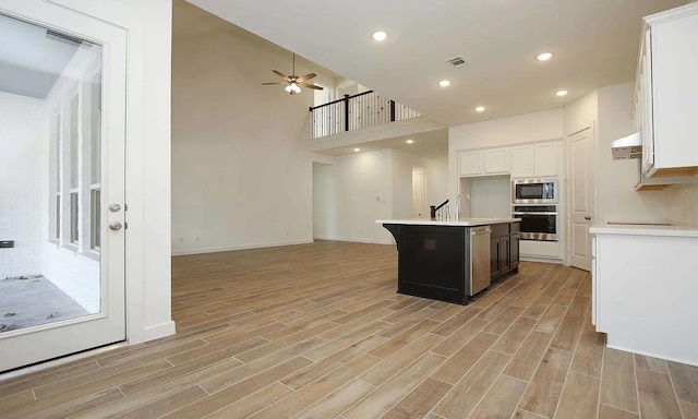 kitchen featuring ceiling fan, light wood-type flooring, white cabinetry, an island with sink, and stainless steel appliances