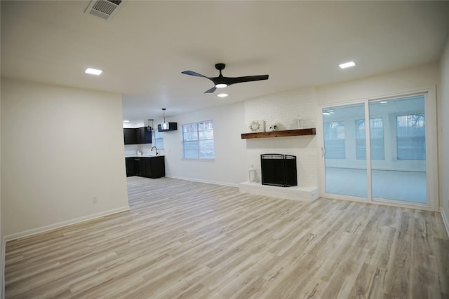 unfurnished living room with ceiling fan, light hardwood / wood-style floors, sink, and a brick fireplace