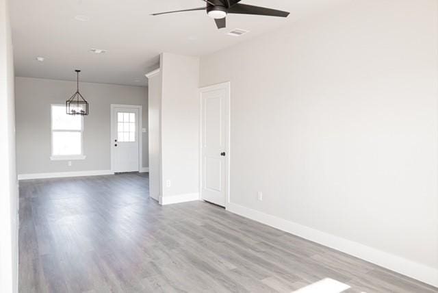 empty room with light hardwood / wood-style floors and ceiling fan with notable chandelier