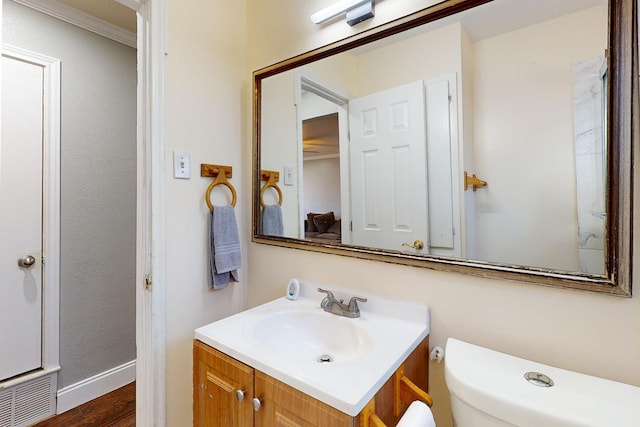 bathroom featuring vanity, wood-type flooring, ornamental molding, and toilet