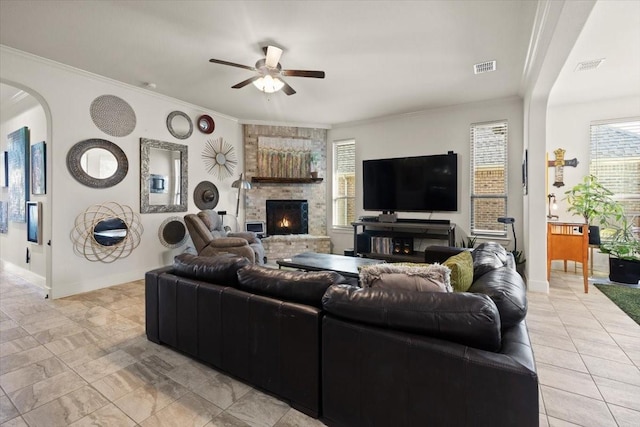 living room with crown molding, a stone fireplace, and a healthy amount of sunlight