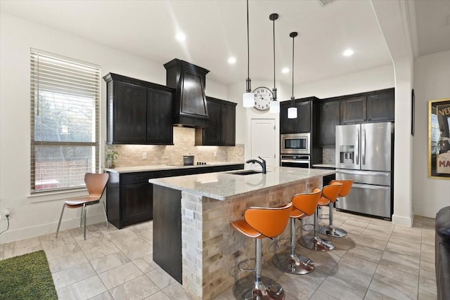 kitchen featuring pendant lighting, a breakfast bar area, appliances with stainless steel finishes, light stone counters, and a center island with sink