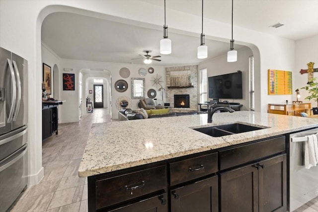 kitchen featuring appliances with stainless steel finishes, pendant lighting, sink, dark brown cabinetry, and light stone counters