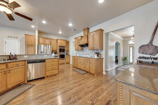 kitchen featuring stone counters, appliances with stainless steel finishes, backsplash, custom range hood, and light hardwood / wood-style flooring