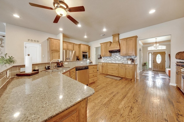 kitchen featuring sink, backsplash, stainless steel appliances, custom exhaust hood, and light wood-type flooring