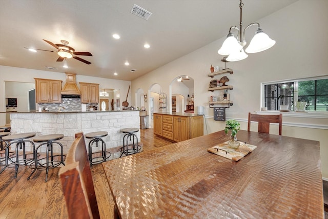 dining space with ceiling fan with notable chandelier and light hardwood / wood-style flooring