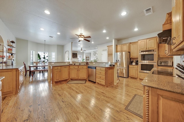 kitchen with light hardwood / wood-style flooring, hanging light fixtures, range hood, stainless steel appliances, and kitchen peninsula